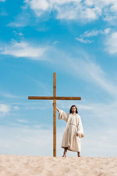 砂漠の砂の上に木製の十字架で立っているあごひげの男 — ストック写真