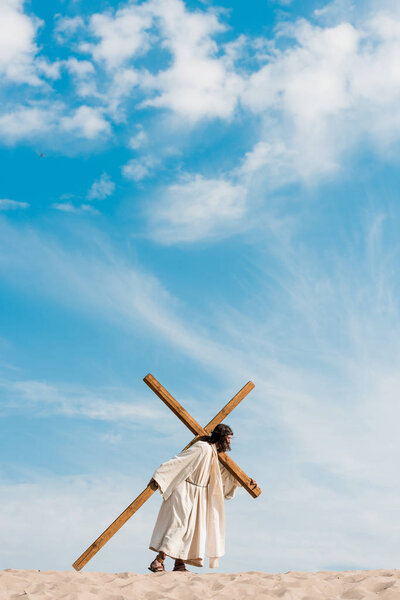 bearded man walking with wooden cross in desert on golden sand 