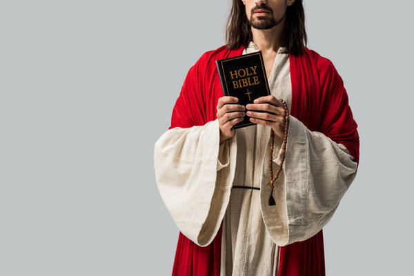 обрезанный вид религиозного человека в одежде Иисуса, держащего священную Библию изолированной на сером
