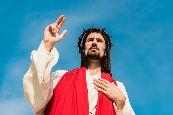 low angle view of man with hand on chest gesturing against blue sky 