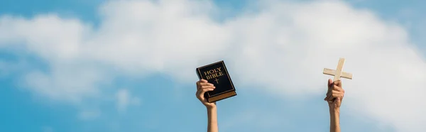 聖書を持ち 雲と青空に対して十字架を持つ男のパノラマショット — ストック写真