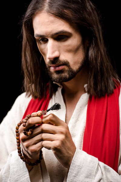 man looking at rosary beads isolated on black 