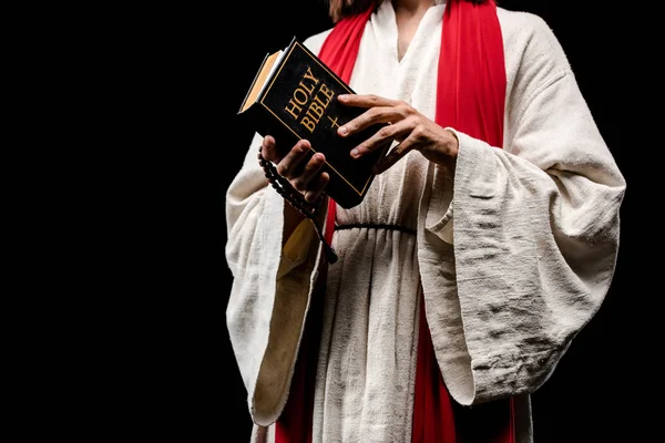 裁剪视图的人拿着书与神圣的圣经字母孤立在黑色 — 图库照片