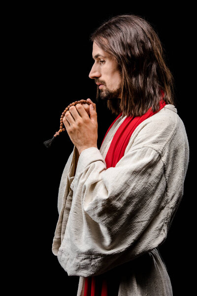 side view of religious man holding rosary beads isolated on black 