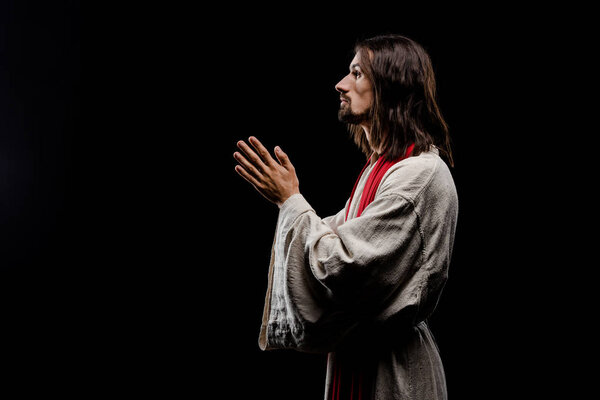 side view of man with praying hands isolated on black 