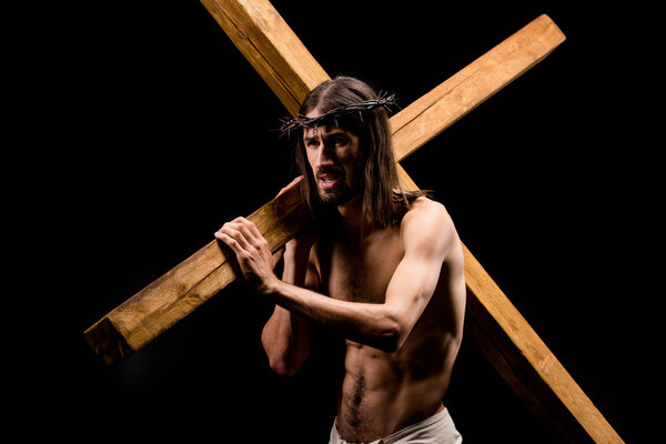 jesus in wreath with spikes holding heavy wooden cross isolated on black 