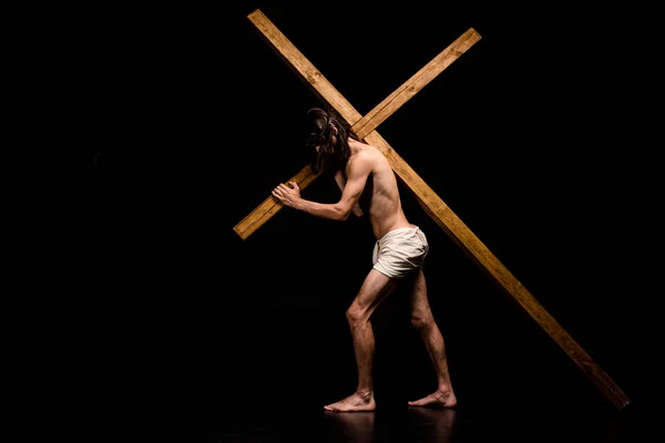 黒の上に木製の十字架で歩くシャツなしのイエス — ストック写真