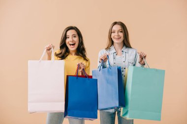 bej izole alışveriş çantaları tutan çekici ve gülümseyen arkadaşlar