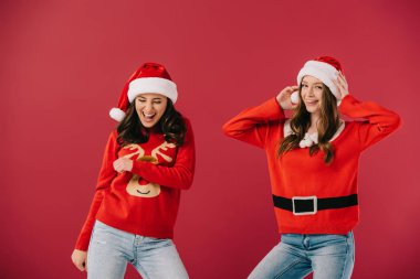 kırmızı izole kamera bakarak kazak ve santa şapkalı çekici ve gülümseyen kadınlar 
