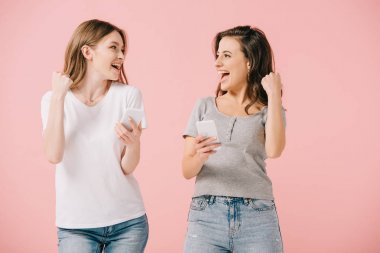 çekici ve gülümseyen kadınlar t-shirt akıllı telefonlar tutan ve evet jest gösteren pembe izole