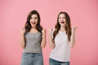 attractive and shocked women in t-shirts looking at camera and showing yes gestures isolated on pink clipart