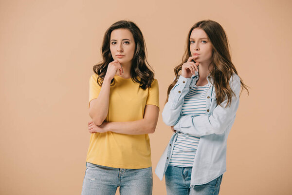 attractive and skeptical friends looking at camera isolated on beige 