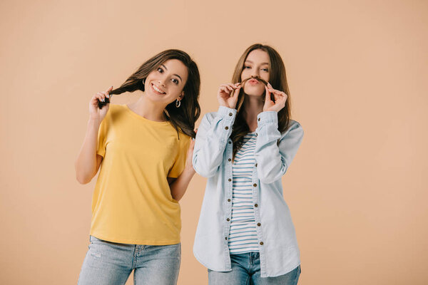 привлекательные и молодые друзья играют с волосами, изолированными от бежевого цвета
