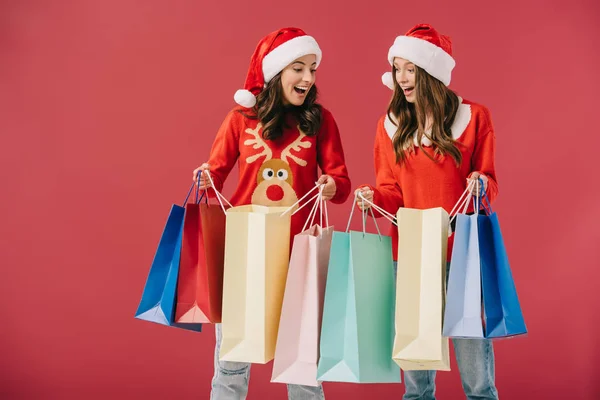 Aantrekkelijk Geschokt Vrouwen Truien Santa Hoeden Houden Boodschappentassen Geïsoleerd Rood — Stockfoto