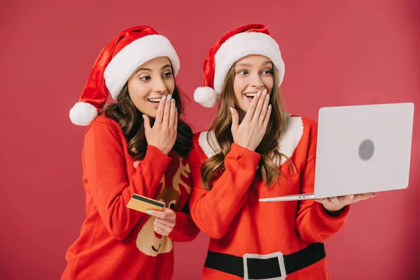 有吸引力的和微笑的妇女毛衣和圣诞老人拿着笔记本电脑和信用卡孤立的红色 — 图库照片