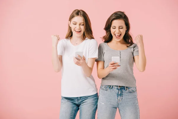 Aantrekkelijke Lachende Vrouwen Shirts Houden Smartphones Tonen Gebaar Geïsoleerd Roze — Stockfoto