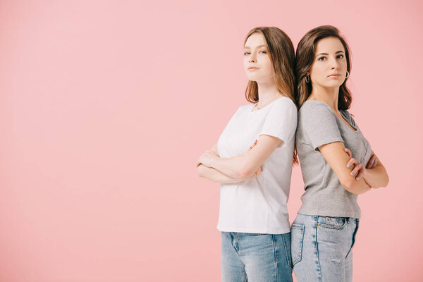 attractive women in t-shirts showing with crossed arms looking at camera isolated on pink