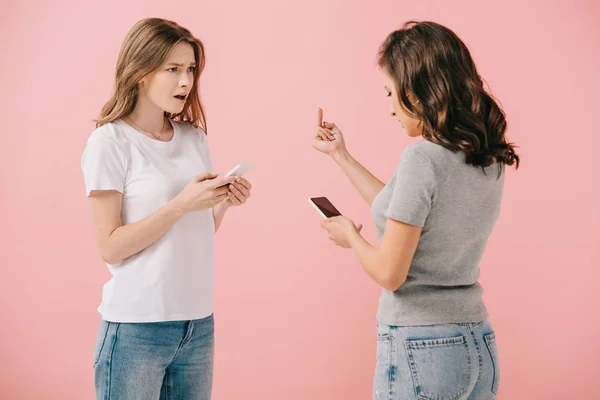 女人在T恤拿着智能手机 并显示中指她的朋友隔离在粉红色 — 图库照片