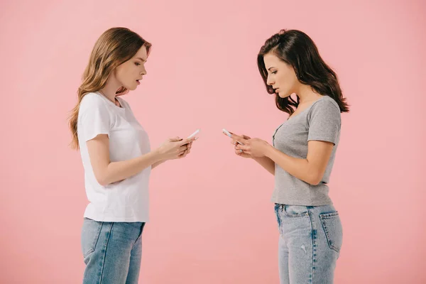 侧视图的吸引力和震惊的妇女在T恤使用智能手机隔离在粉红色 — 图库照片
