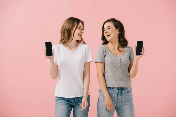Χαμογελαστές Και Ελκυστικές Γυναίκες Μπλουζάκια Που Κρατούν Smartphones Απομονωμένα Ροζ — Φωτογραφία Αρχείου