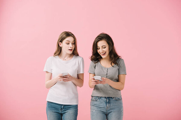 attractive and smiling women in t-shirts holding smartphone isolated on pink