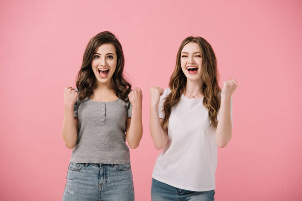 привлекательные и шокированные женщины в футболках, смотрящие в камеру и показывающие жесты "да", изолированные на розовом
