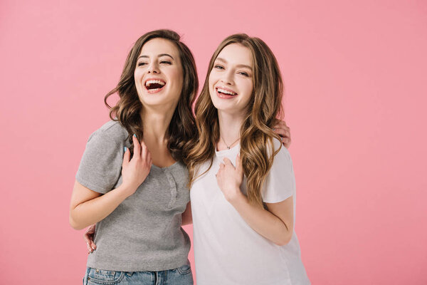 attractive and smiling women in t-shirts looking at camera isolated on pink