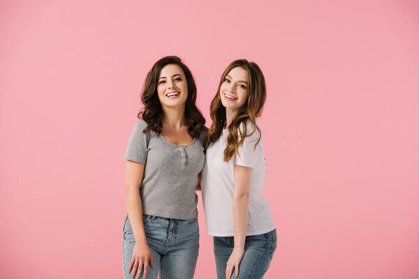 attractive and smiling women in t-shirts looking at camera isolated on pink