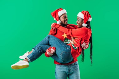 Kırmızı Noel kazak ve Santa şapka lı Afro-Amerikan adam yeşil izole kadın gülümsedi kadar tutarak