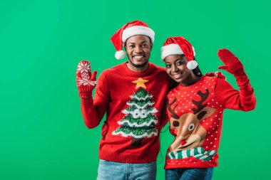 Kırmızı Noel süveter ve Noel Baba şapkalı Afro-Amerikalı çift el sallıyor ve yeşil kameraya bakıyor.