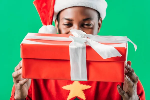 在圣诞老人帽子的非洲裔美国人拿着红色的礼物盒与白色丝带隔离在绿色 — 图库照片