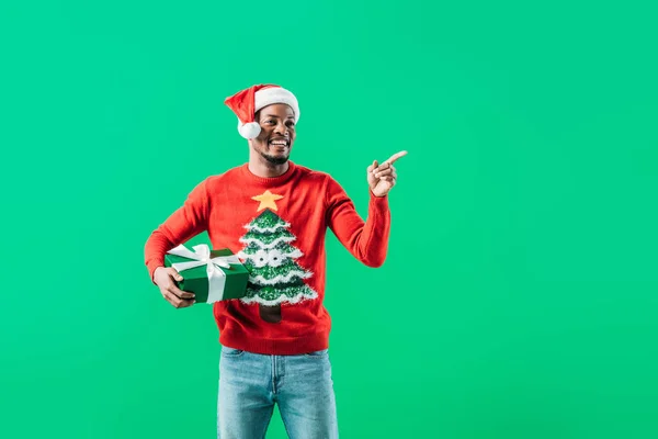 African American Man Christmas Sweater Santa Hat Holding Present Pointing — Stock Photo, Image