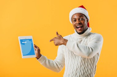 Kiev, Ukrayna - 2 Ağustos 2019: Noel Baba şapkalı Afro-Amerikan adam sarı izole twitter uygulaması ile dijital tablet parmak ile işaret