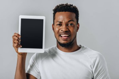 boş ekran ile dijital tablet tutan ve gri izole kamera bakarak üzgün Afrikalı Amerikalı adam