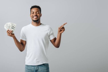 African American man holding dollar banknotes and point with finger isolated on grey