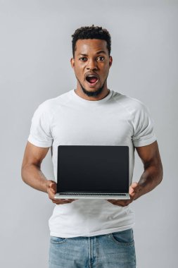 boş ekran ile dizüstü bilgisayar gösteren ve gri izole kamera bakarak şok Afrikalı Amerikalı adam