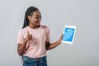 Kiev, Ukrayna - 2 Ağustos 2019: Twitter uygulaması ile dijital tablet tutan ve gri izole başparmak gösteren Afrikalı Amerikalı kadın