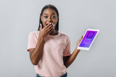 Alışveriş uygulaması ile dijital tablet tutan ve gri izole el ile ağız kapsayan Afrikalı Amerikalı kadın
