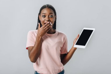 Boş ekranlı dijital tablet tutan ve ağzı gri ye bağlı el ile kaplayan Afro-Amerikalı kadın