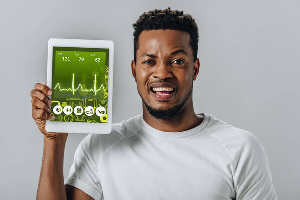 расстроен афроамериканец держит цифровой планшет с фитнес-приложений и глядя на камеру изолированы на серый
