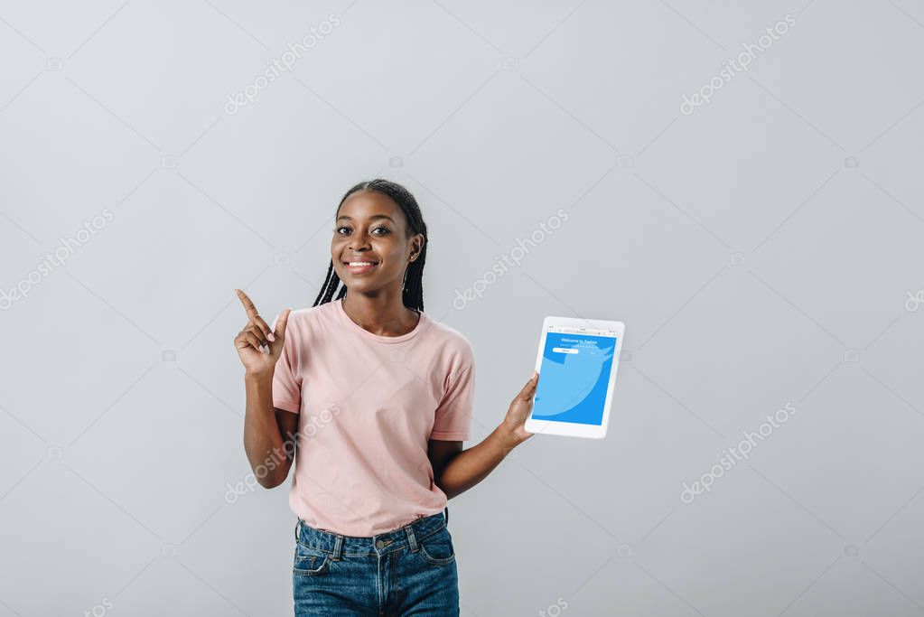 KYIV, UKRAINE - AUGUST 2, 2019: African American woman holding digital tablet with twitter app and pointing with finger isolated on grey