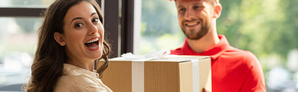panoramic shot of happy woman receiving carton box from cheerful delivery man 