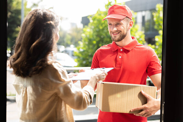 woman giving clipboard to happy delivery man with box 