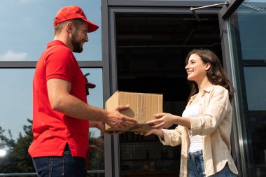 handsome delivery man giving cardboard box to cheerful woman  clipart