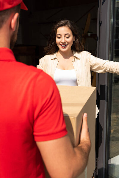 cropped view of delivery man holding carton box near pretty girl 