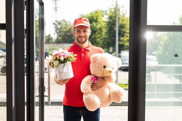 happy delivery man holding teddy bear and flowers 