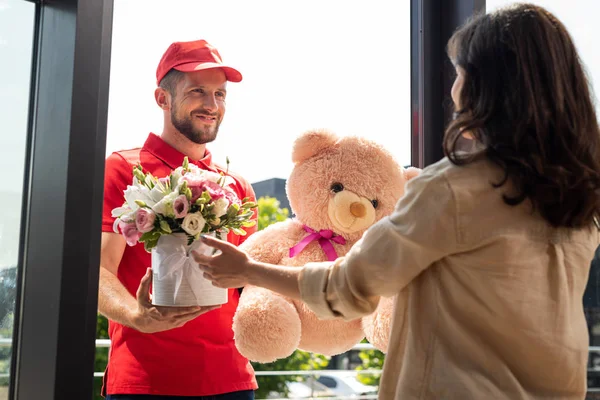 Selective Focus Cheerful Delivery Man Holding Teddy Bear Flowers Woman — Stock Photo, Image
