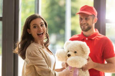 selective focus of positive girl receiving teddy bear from bearded man in cap  clipart