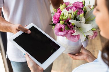 kadına boş ekranile çiçek ve dijital tablet veren teslimat adam kırpılmış görünümü 