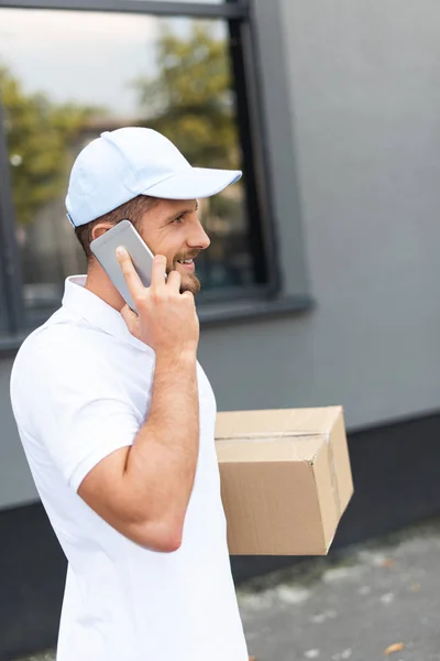 Cheerful Bearded Delivery Man Talking Smartphone While Holding Box — Stock Photo, Image